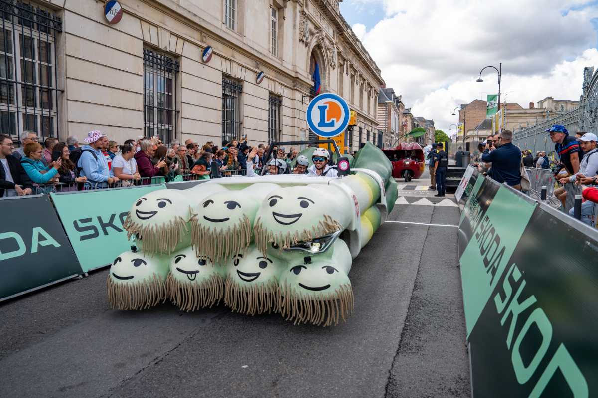 Char Poireau de la caravane E.Leclerc sur le Tour de France, salué par les spectateurs souriants au bord de la route.