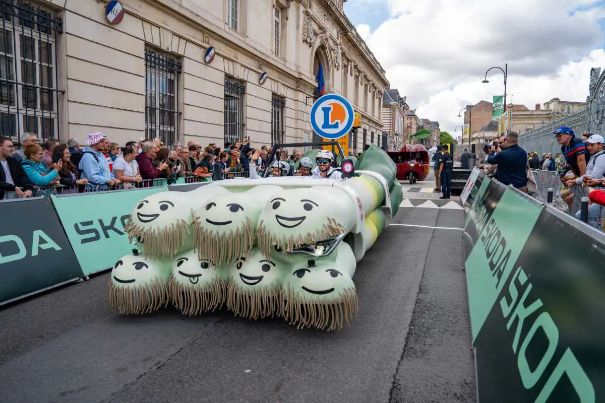Char Poireau de la caravane E.Leclerc sur le Tour de France, salué par les spectateurs souriants au bord de la route.